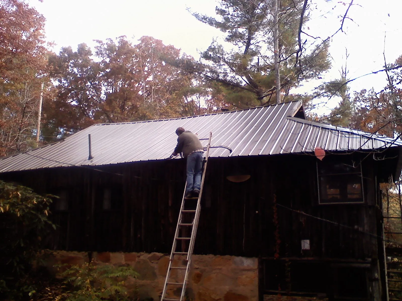 Roofer on a ladder working along the edge of a cabin metal roof in Yorkville